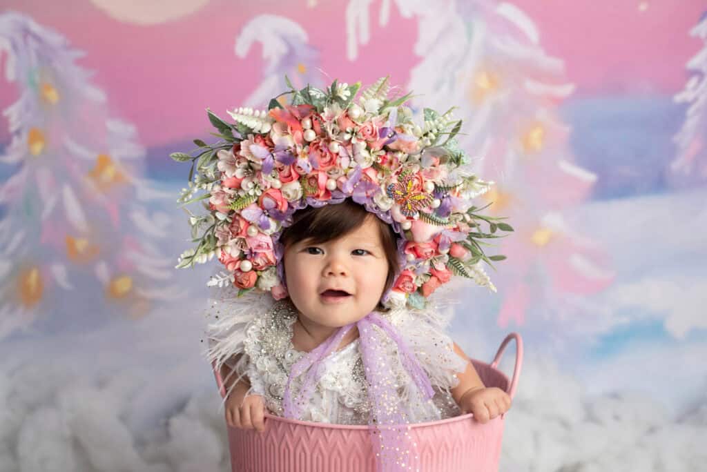 A baby in a pink bucket wearing a flower crown.