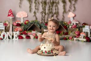 A baby girl sitting in front of a cake in front of a forest.
