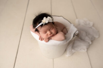 A baby girl is laying in a bucket on a wooden floor.