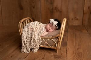 A newborn girl in a wicker basket on a wooden floor.