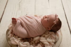 A newborn wrapped in a pink blanket on a wooden table.
