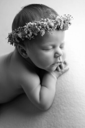A black and white photo of a baby wearing a flower crown.