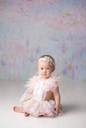 A baby girl in a pink dress sitting on a white background.