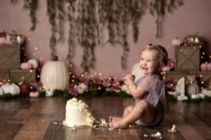 A baby girl is sitting on the floor with a cake in front of her.