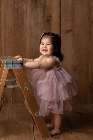 A little girl in a pink dress is standing on a wooden ladder.