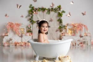 A baby girl is sitting in a bath tub with butterflies.