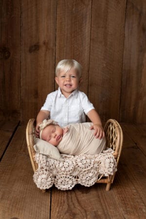 A boy and a newborn sitting in a wicker basket.