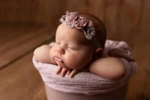 A baby girl is sleeping in a pink bucket.