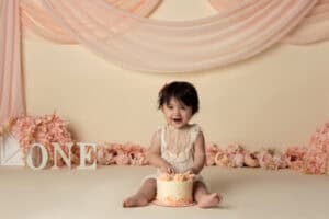 A baby girl is sitting in front of a cake with the number one on it.