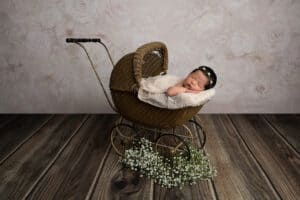 A newborn baby in a wicker carriage with flowers.