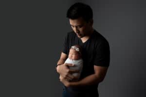 A man holding a baby on a grey background.