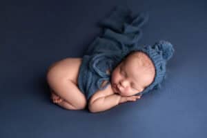 A newborn baby sleeping on a blue background.