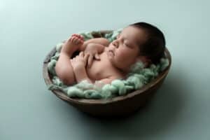 A baby boy is sleeping in a bowl on a green background.