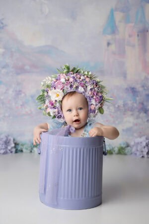 A baby sitting in a purple bucket with a flower crown.