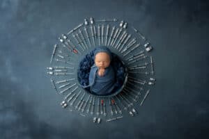 A newborn baby in a blue blanket surrounded by a circle of syringes.