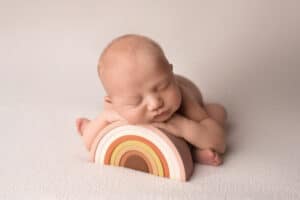A baby boy laying on top of a wooden rainbow.