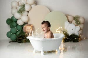 A baby in a bath tub with balloons and greenery.
