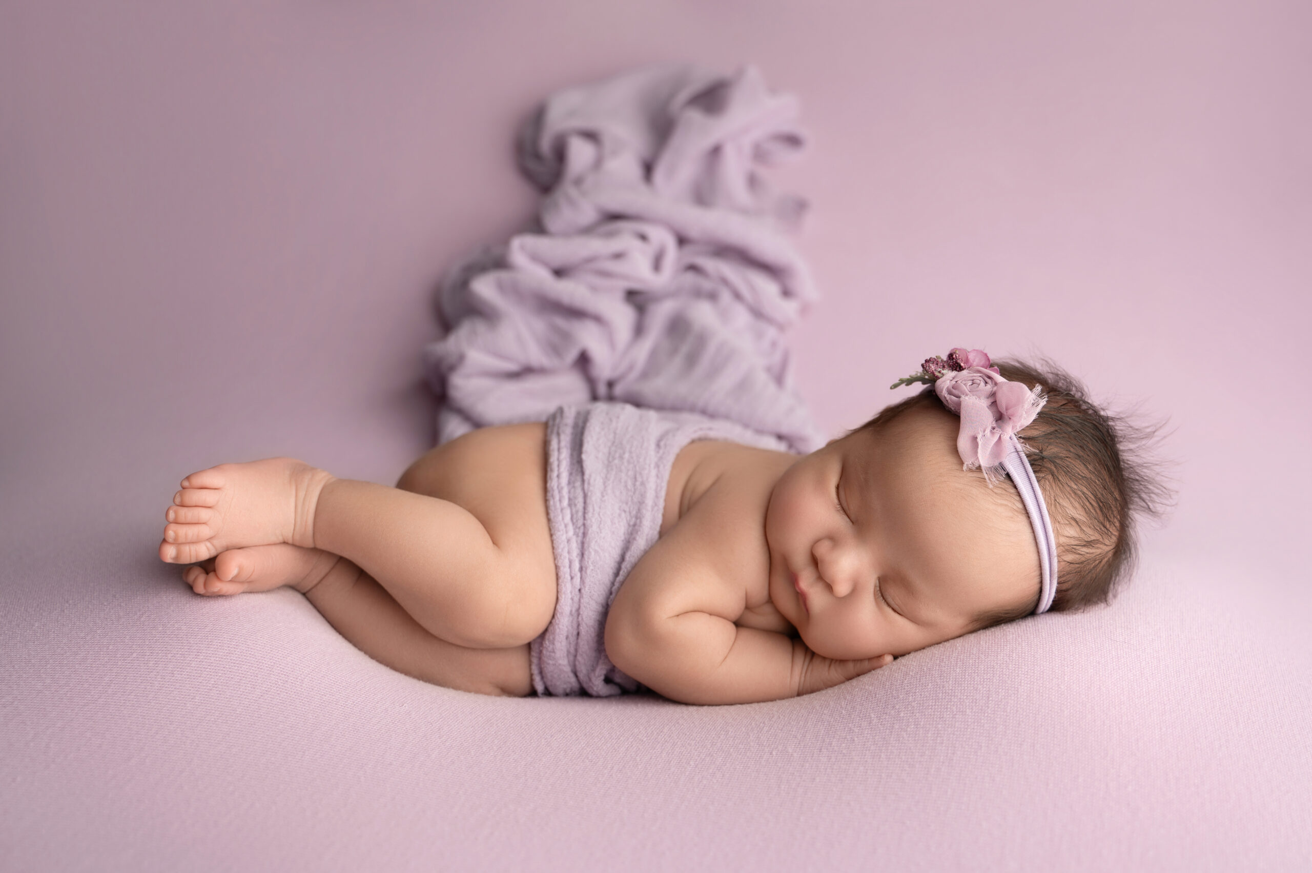 a sleeping baby lies on a soft purple blanket, wrapped in matching hues, with a floral headband. the peaceful setting conveys a serene and tender atmosphere, much like following an investment guide that promises secure futures and tranquility.
