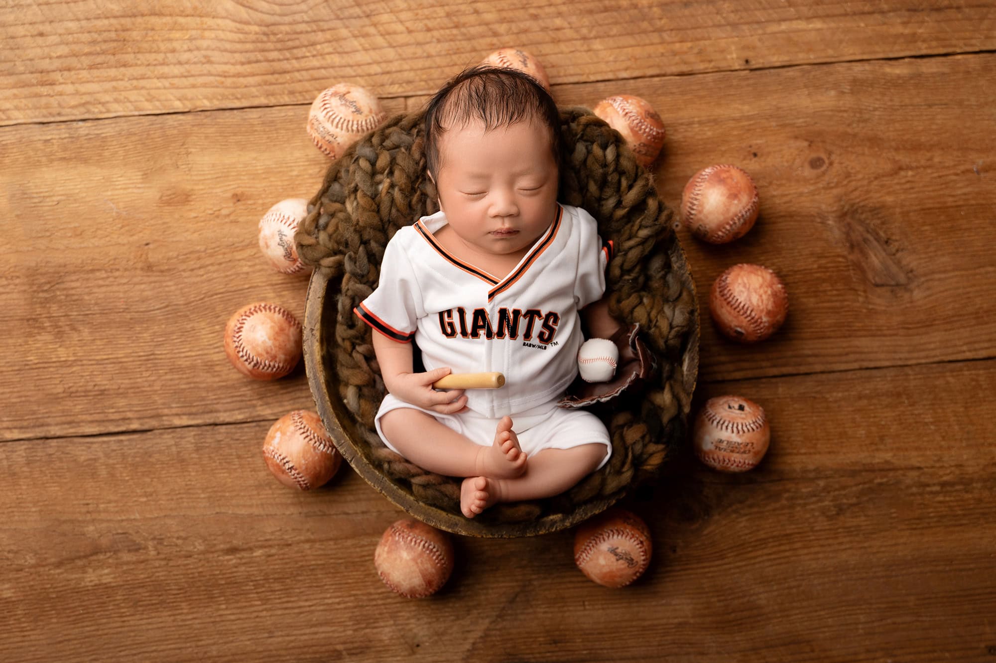 Sleeping baby in baseball outfit with baseballs.