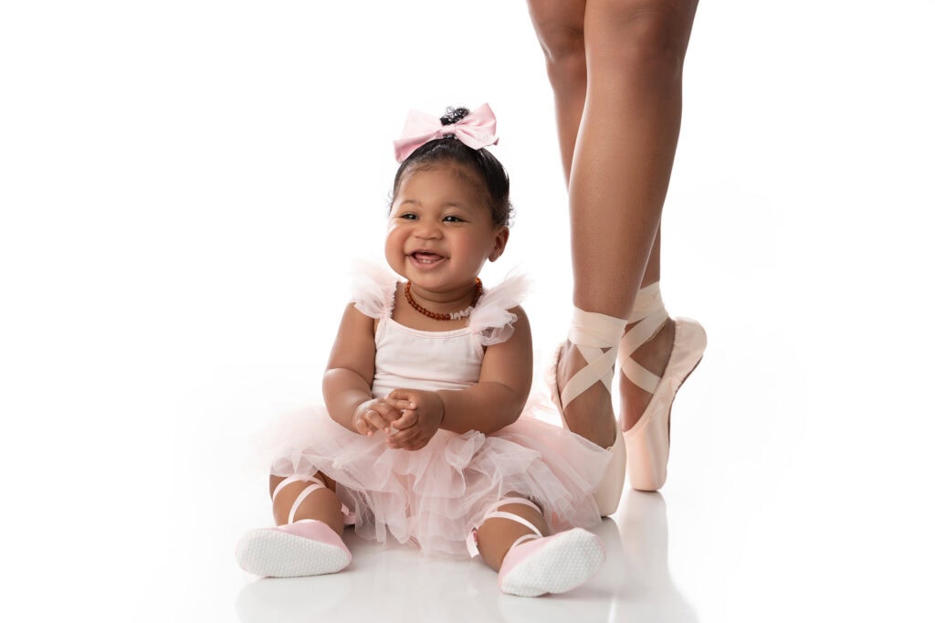 Smiling baby in ballet outfit with ballerina's legs.