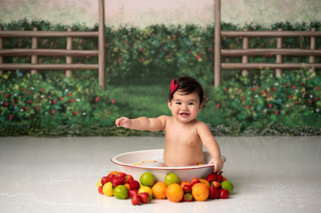 Smiling baby in tub surrounded by fruits.