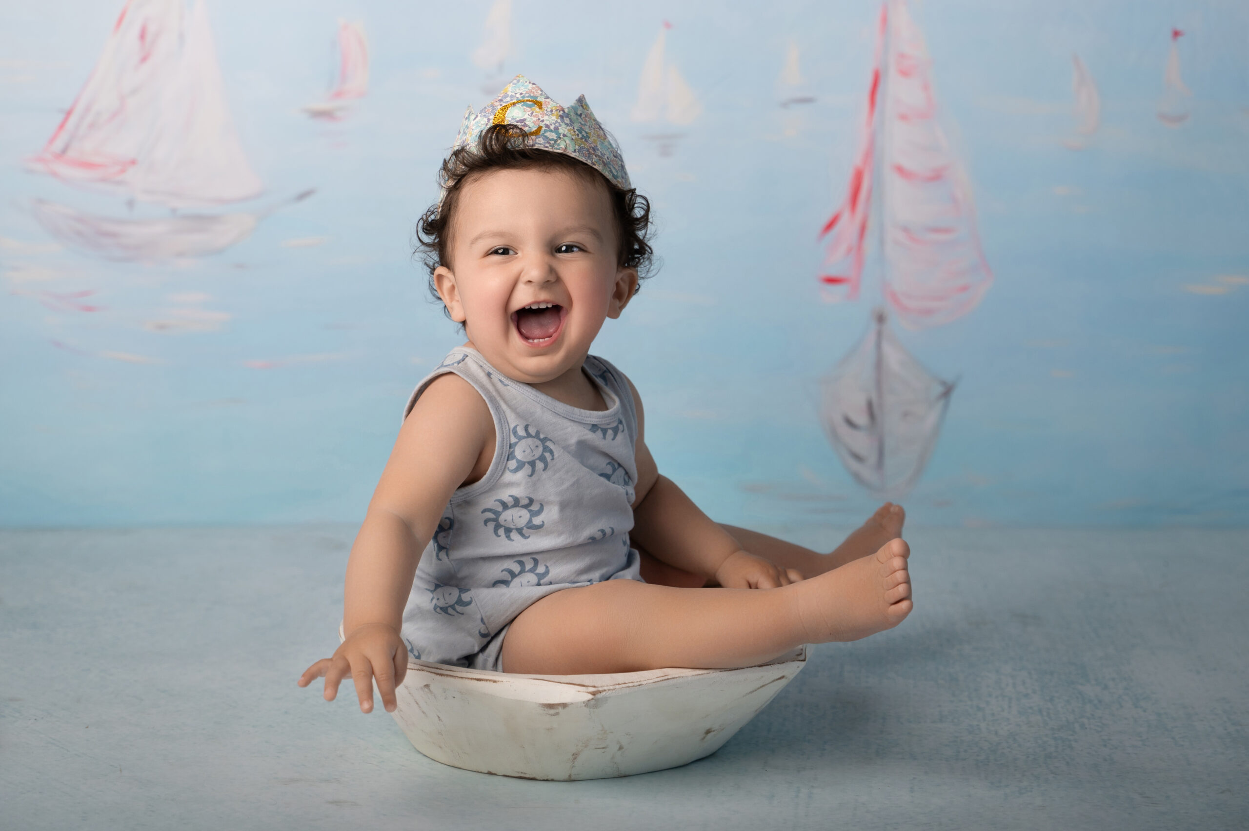 Smiling baby in sailor-themed photoshoot with painted sailboats.