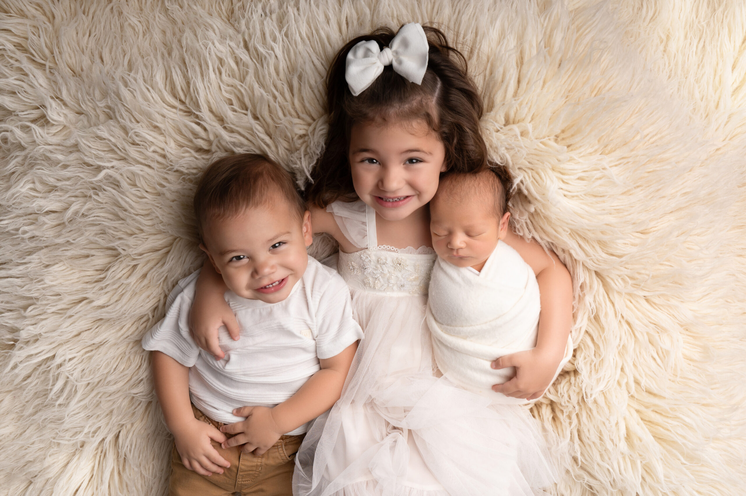 Smiling siblings with newborn on fuzzy blanket
