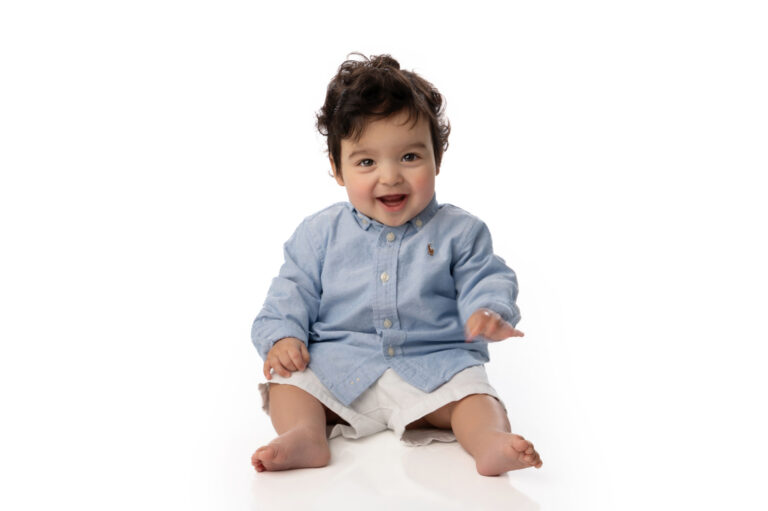 Smiling baby in blue shirt sitting on white background